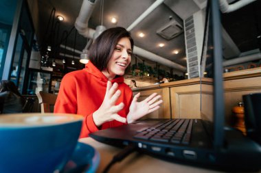 Young woman at the bar having a coffee and using a laptop clipart