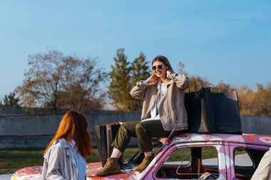 Genç kadınlar eski bir arabanın yanında poz veriyorlar.