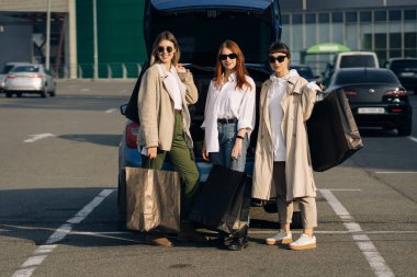 Alışveriş torbalarıyla arabada genç kadınlar var.