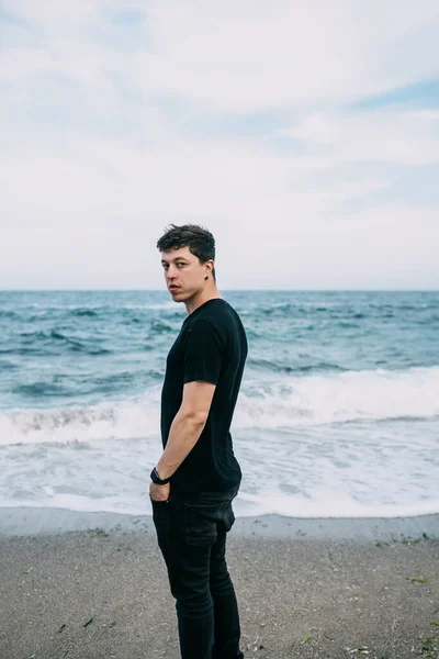Улыбающийся парень в черной футболке стоит на песчаном берегу. — стоковое фото