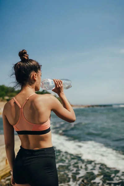 Wanita minum air tawar dari botol setelah latihan di pantai — Stok Foto