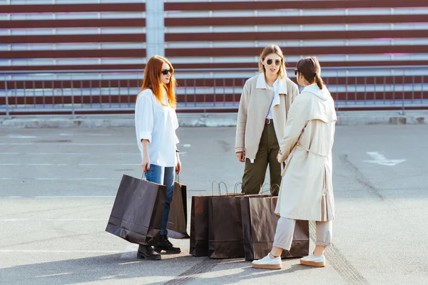 Elinde çantaları olan genç kadınlar kameraya poz veriyor.