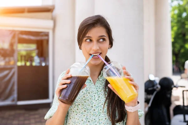 Mujer joven bebe dos cócteles con hielo en vasos de plástico con paja —  Fotos de Stock