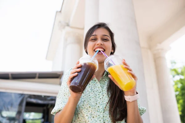 Wanita muda minum dua koktail dengan es di cangkir plastik dengan jerami — Stok Foto