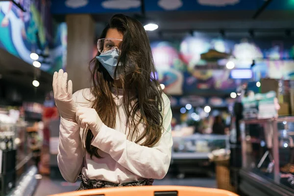 Женщина в хирургической маске и перчатках ходит по магазинам в супермаркете — стоковое фото