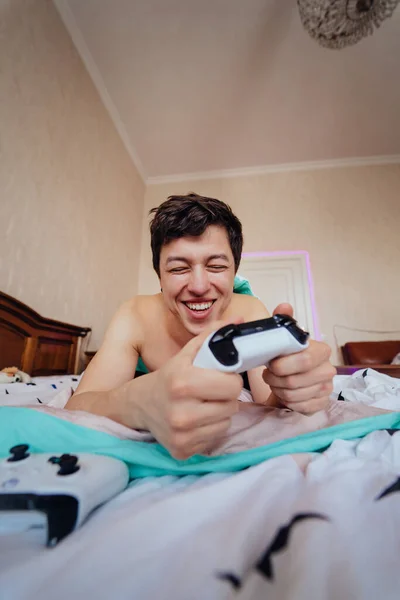 Парень лежит в постели и играет в видеоигры, держа контроллер — стоковое фото