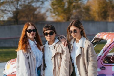 Genç kadınlar eski bir arabanın yanında poz veriyorlar.