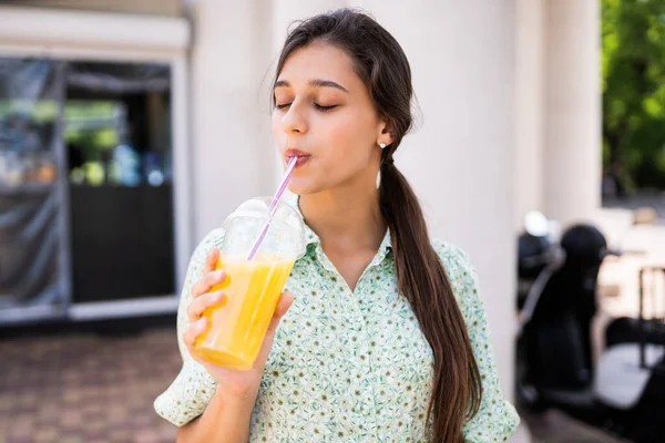 Mujer joven sonriendo y bebiendo cóctel con hielo en taza de plástico con paja — Foto de Stock