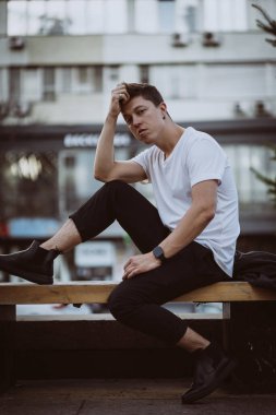 Şehir caddesinde oturan adam, kameraya bak ve etrafına bak.