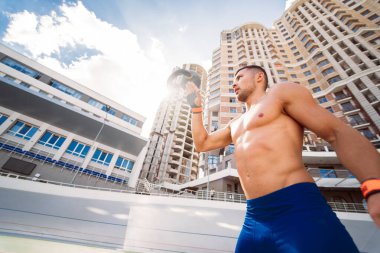 Yüksek bir binanın arka planında kettlebell ile antrenman yapan sporcu..