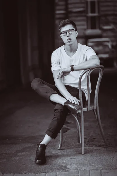 Портрет мужчины, сидящего на стуле в белой футболке и солнцезащитных очках на улице — стоковое фото
