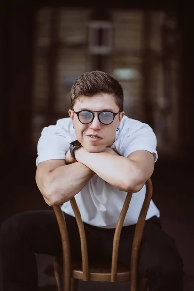 Portrait d'hommes assis sur une chaise avec t-shirt blanc et lunettes de soleil dans la rue — Photo