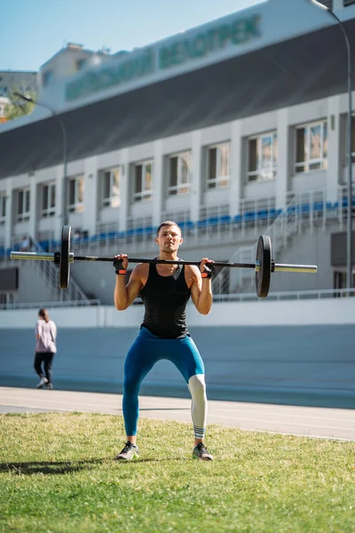 Young guy raises the bar in the stadium, outdoor workout