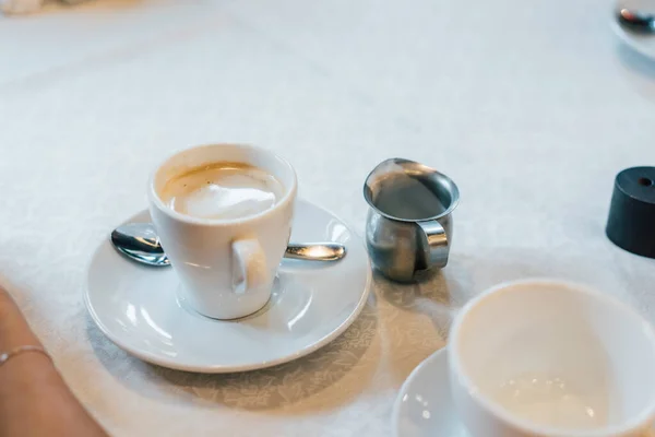 Mała biała filiżanka cappuccino stoi na stole — Zdjęcie stockowe