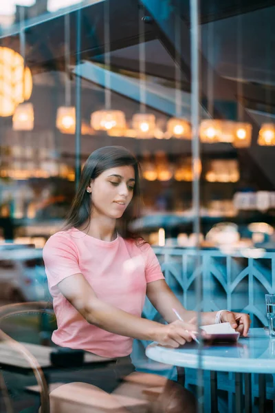 Beautiful brunette sitting behind a window in a cafe bar. — Stock Photo, Image