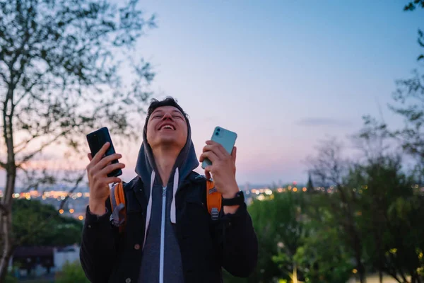 Młody facet w parku robi zdjęcie na dwóch smartfonach — Zdjęcie stockowe