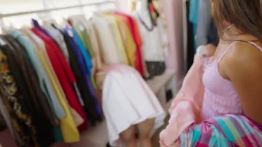 İki kadın şık bir butikte renkli ve canlı bir elbise rafından hevesle kıyafet seçiyor.