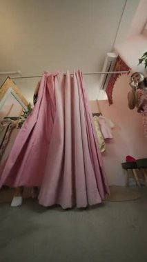 Şık bir kız canlı bir soyunma odasında yumuşak pembe perdelerin arkasında değişik kıyafetler deniyor.