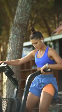 Kendini işine adamış ve odaklanmış bir kadın güzel bir doğal ortamda eliptik bir makine üzerinde yoğun bir çalışma yapar.
