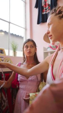 İki şık kadın renkli kıyafetler ve şık aksesuarlarla dolu bir butiği zevkle keşfediyorlar.