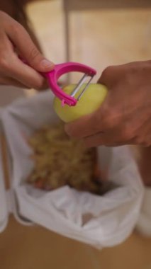 Bir insan dikkatlice renkli bir meyveyi soyuyor ve kabuğunu dikkatlice çöp kutusuna atıyor.