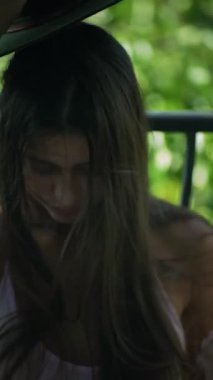 Yumuşak, dalgalı bir yaz elbisesi giymiş genç bir kadın şık bir şapka giyerken zarif bir şekilde dışarıda poz veriyor.