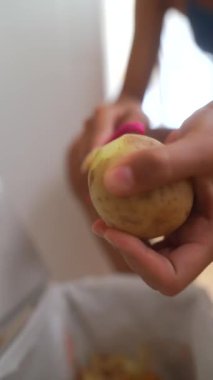 Bir insan patatesi dikkatlice soyar, kabuklarını yakındaki bir çöp kutusuna atar, yemek hazırlama çabalarını ön plana çıkarır.