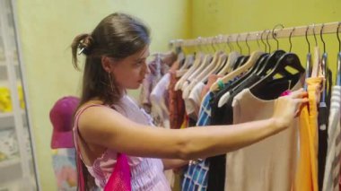 Genç bir kadın renkli bir butikte şık giysiler keşfediyor, modern moda eğilimlerini sergiliyor.