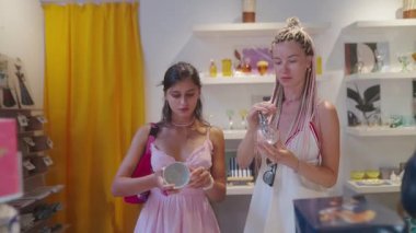 İki genç kadın, benzersiz el sanatları ve çeşitli güzellik ürünleri arayışında bir zanaatkar dükkanını zevkle keşfediyor.