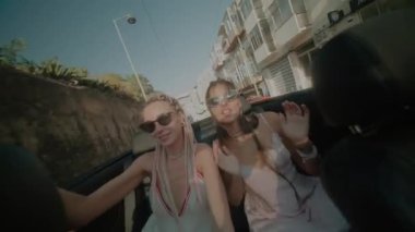 İki modaya uygun arkadaş güneşli gökyüzünün altında üstü açık bir arabada keyifle eğleniyor.