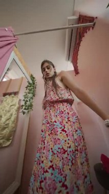 Zarif bir kadın şık bir çiçekli elbisenin modelliğini yaparken büyüleyici bir şekilde dekore edilmiş ve rahat bir odada duruyor.