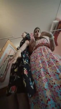 İki arkadaş, neşe ve neşe dolu elbiselerini neşe ve neşe dolu bir soyunma odasında sergiliyorlar.