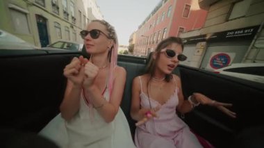 İki arkadaş güneşin altında üstü açık bir arabada heyecanlı bir gezinti yapıp, birlikte mutlu anları yakalıyorlar.