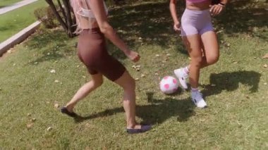 Güneşli bir günde parkta futbol oynamaktan zevk alan iki kadın, oyunculuk ve etkinlik sergiliyor..