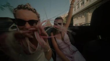 Güneşli ve güzel bir günde üstü açık bir arabada neşeli bir kutlama yapan iki arkadaş.