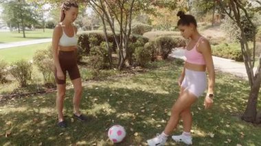 İki yakın arkadaş güneşli, canlı bir park alanında birlikte futbol oynayarak eğleniyorlar.