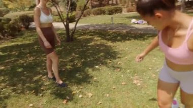 İki arkadaş parlak ve güneşli bir günün keyfini çıkarırken aynı zamanda canlı bir park ortamında birlikte futbol oynuyorlar.