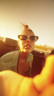 Günbatımında üstü açık şık bir arabanın içinde kaygısız bir an. Yaz neşesi ve mutluluğunun özünü yakalıyor.