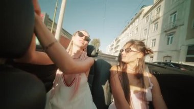 İki arkadaş üstü açık bir arabada güneşli bir sürüşün keyfini çıkarıyorlar, manzarada sırılsıklam sırıtıyorlar ve gülüyorlar.