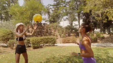 İki arkadaş, güneşli parkta parlak sarı bir topla yakalamaca oynuyorlar. Birlikte yaz günlerinin tadını çıkarıyorlar.