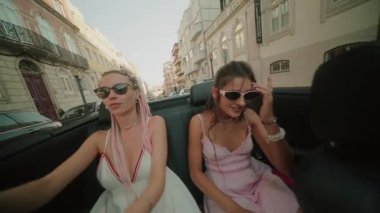 İki şık kadın, güneşin altında üstü açık bir arabada keyifle vakit geçirir ve neşeli bir yaz havası yakalarlar.