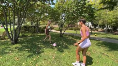İki arkadaş, yaz günü güzel bir parkta güneşin altında futbol oynuyorlar.