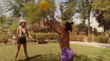 Güneşli bir günde, iki arkadaş neşeli bir şekilde renkli, canlı bir parkta dışarıda top oynuyorlar.