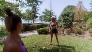 İki arkadaş, doğa ile çevrili yemyeşil bir parkta renkli bir topla dışarıda oynarken eğleniyorlar.