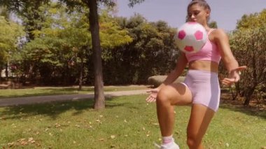 Bir kadın, parlak ve güneşli bir park ortamında çeşitli futbol becerileri çalışırken neşesini ifade eder.