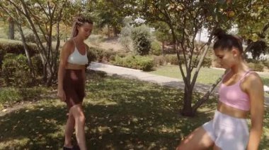 İki aktif kadın neşeli bir şekilde güneşli bir parkta futbol oynuyor. Arkadaşlıklarını ve eğlencelerini sergiliyorlar.