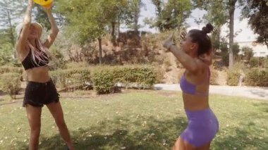 İki yakın arkadaş güneşin altında renkli bir plaj topu kullanarak neşeli bir açık hava fitness aktivitesi yapıyorlar.