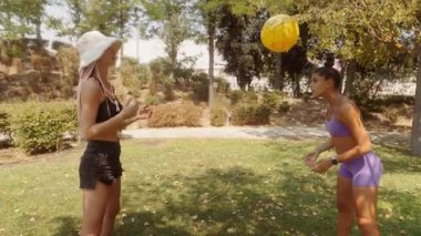 İki arkadaş güneşli bir parkta parlak bir top atarken keyifli ve eğlenceli bir an yaşıyorlar.