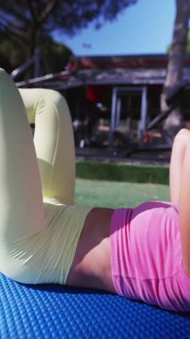 Dinamik ve canlı bir zindelik oturumu. Sıcak güneşin altında canlı aktif giysiler giyerken çekirdek egzersizlerine odaklanıyor.