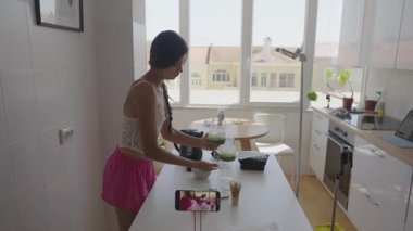 Yetenekli bir kadın, yaratıcılıkla dolu güneşli ve neşeli bir mutfakta canlı malzemelerle sağlıklı meyve suyu yapar.